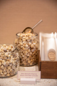 Two glass jars of Miss Hannah's popcorn with a scoop on a table.