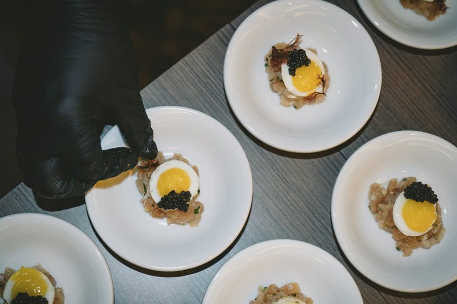 Line of dishes of quail egg being prepped and garnished with dulce seaweed.