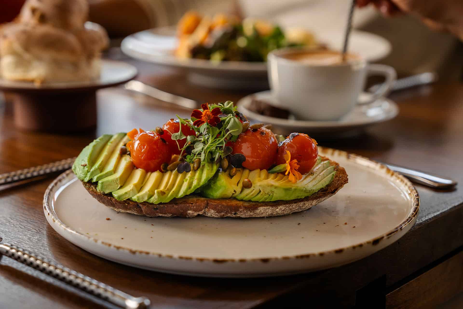 A plate of avocado toast garnished with small tomatoes, seeds, micro greens and edible flowers.