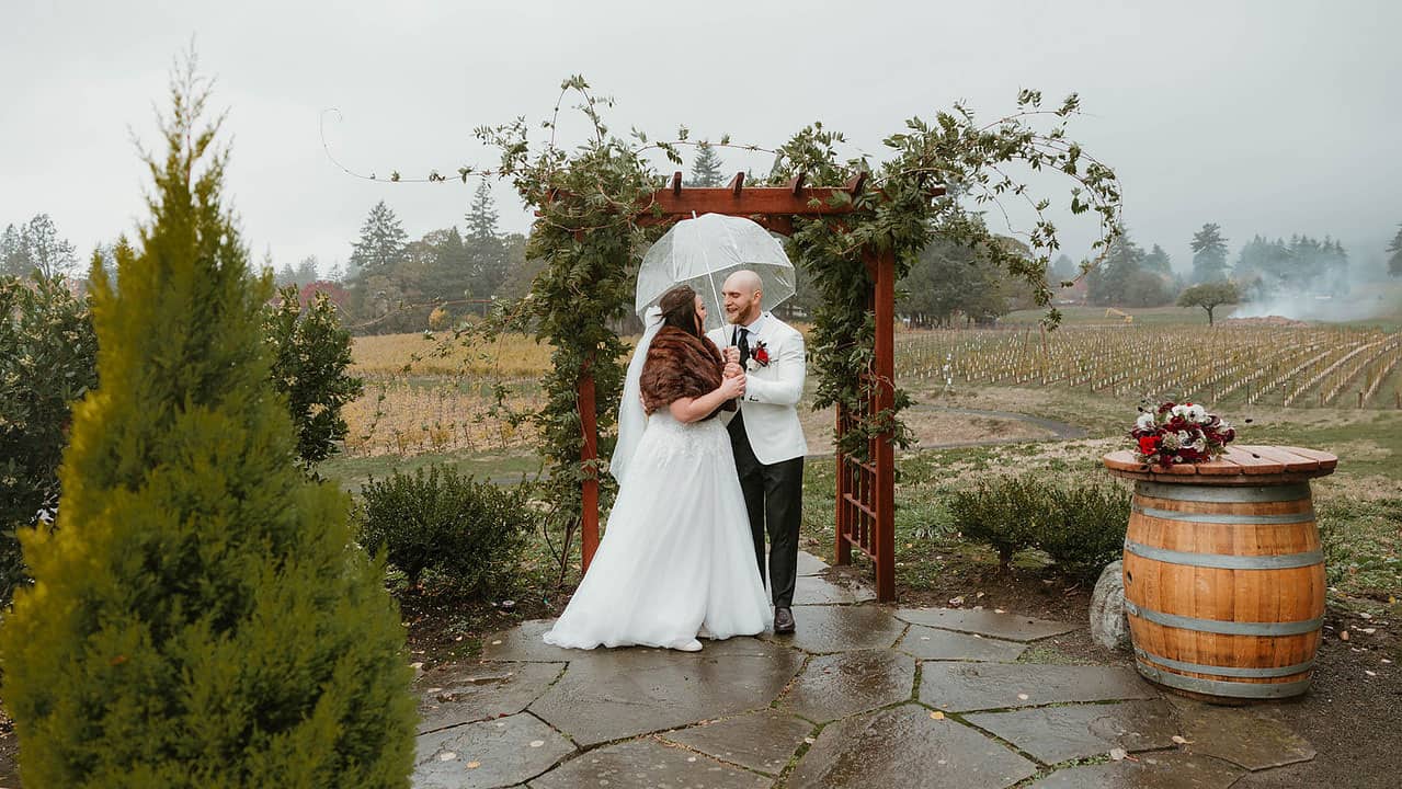 A bride and groom under an umbrella at the Vineyard Overlook on a fall day.