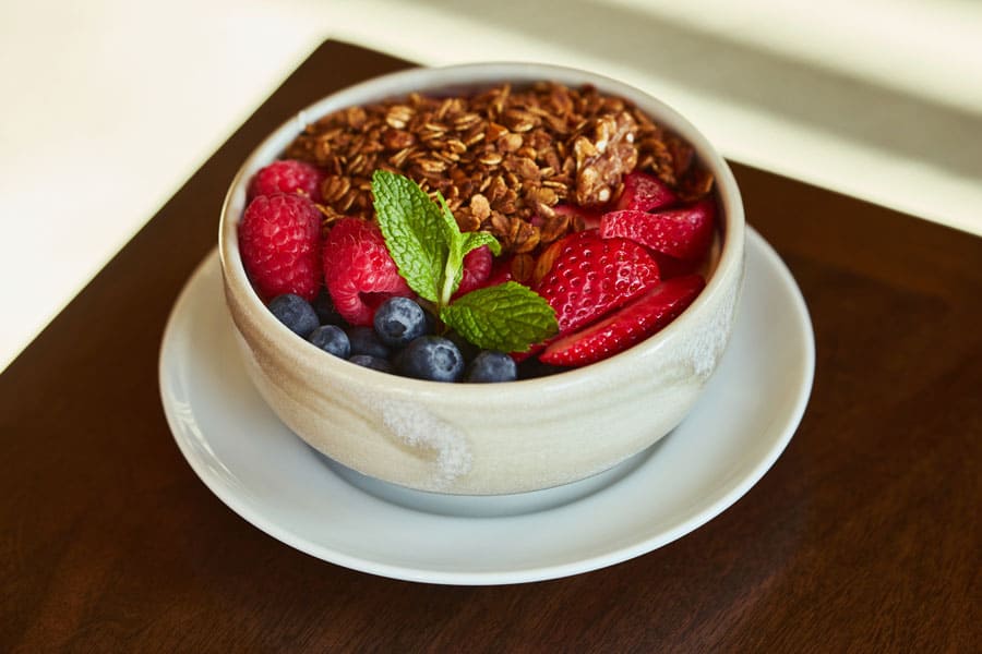 Fruit and granola in a white bowl on top of a table.