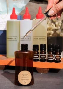 A female hand holding an eye dropper with oil over a blending bottle.