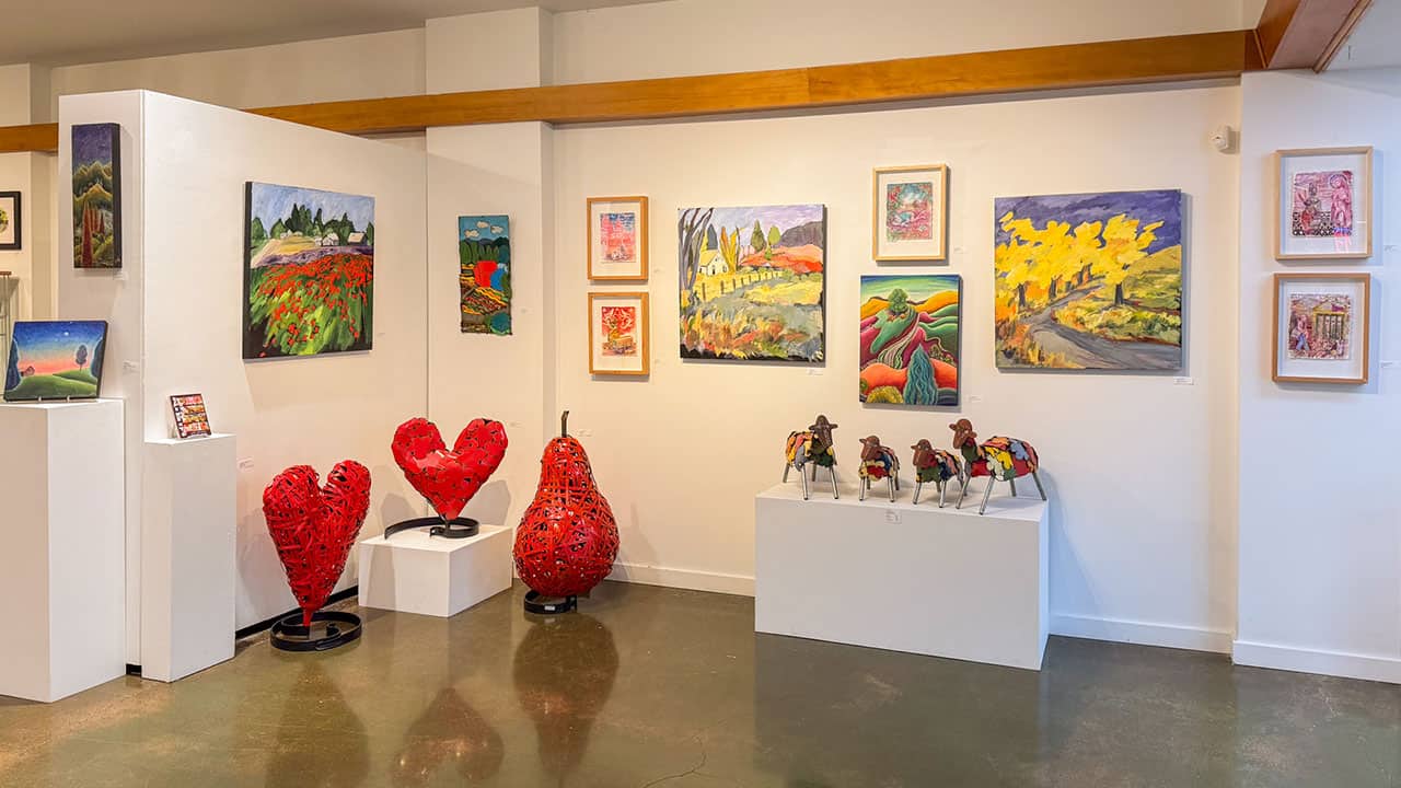 Art exhibit at Art Elements Gallery including metal sculptures of hearts and sheep with vibrant paintings on the wall.