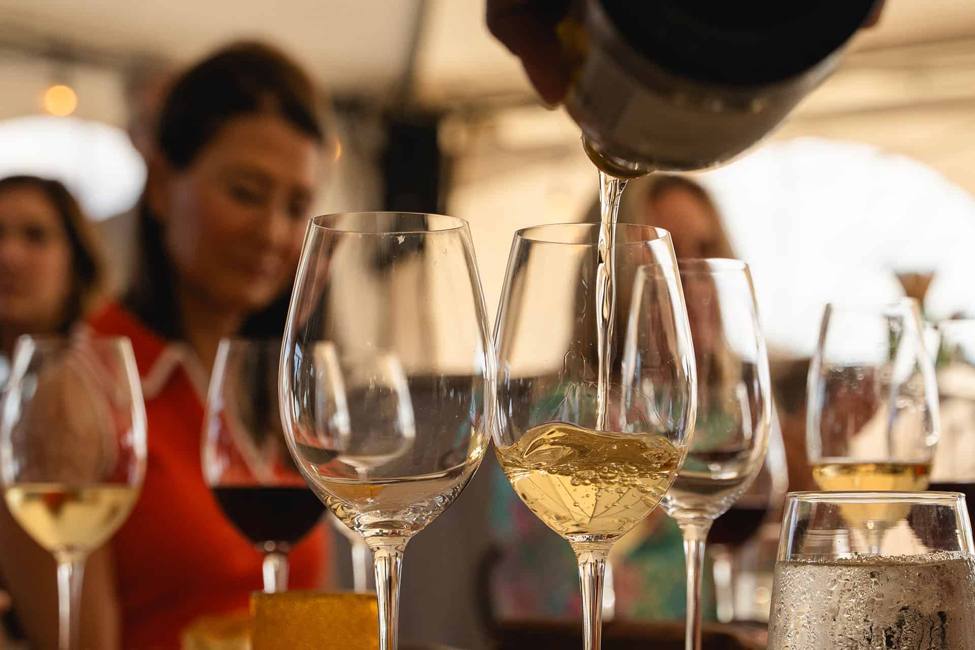 A server pouring white wine in a glass for an attendee at a dinner party in the Chef's Garden.
