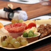 A female guest building a colorful plate of meats, cheeses and fruits.