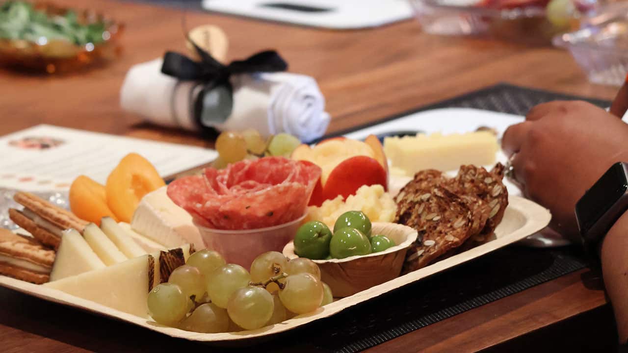 A female guest building a colorful plate of meats, cheeses and fruits.