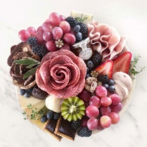 A finished charcuterie board with meets, cheeses, crackers, cookies and fruit.