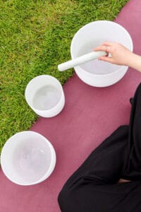 An instructor sitting on a yoga mat performing on three sound bowls.