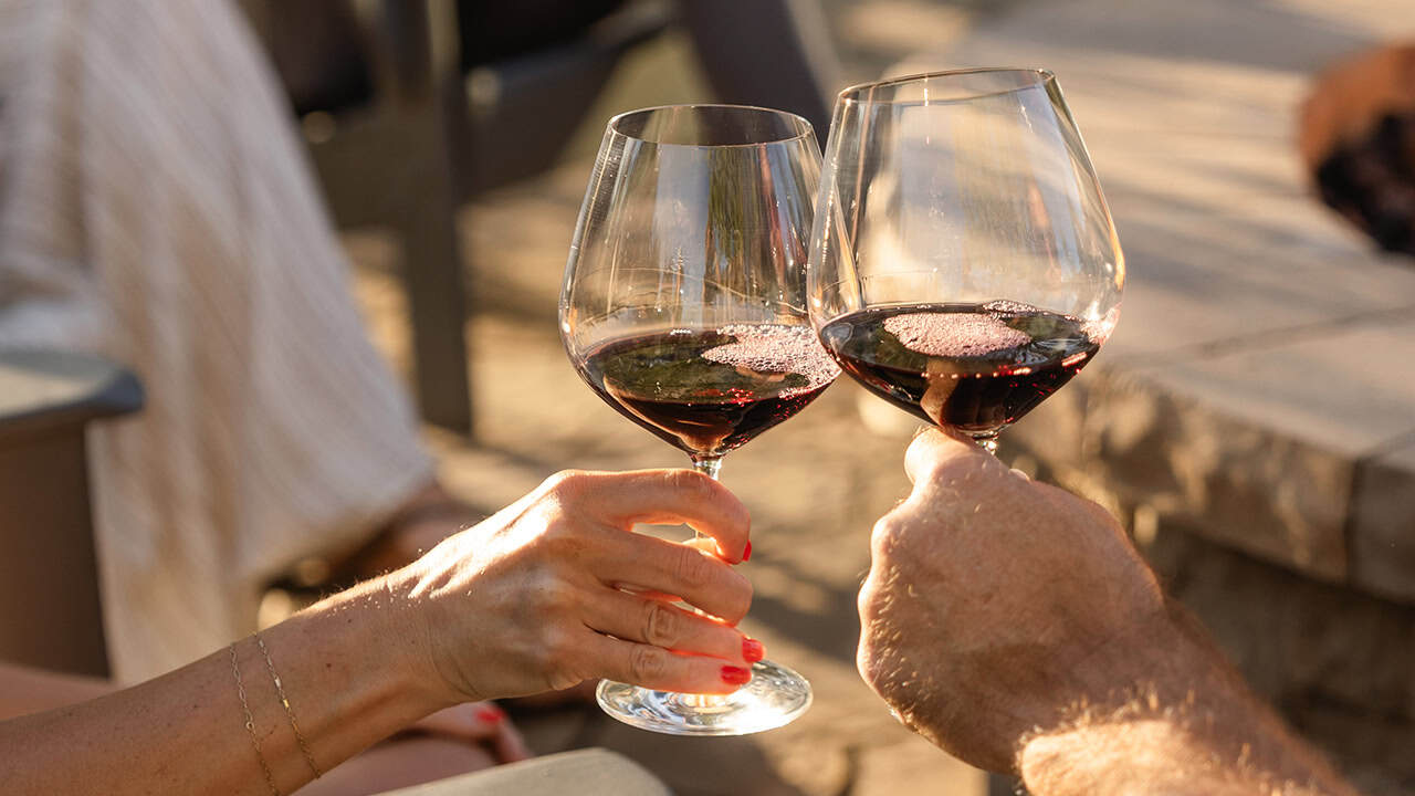 Two guests with glasses of pinot noir sitting by the firepit.