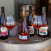 Four bottles of wine from Compris Vineyard and two wine glasses on a wine barrel.