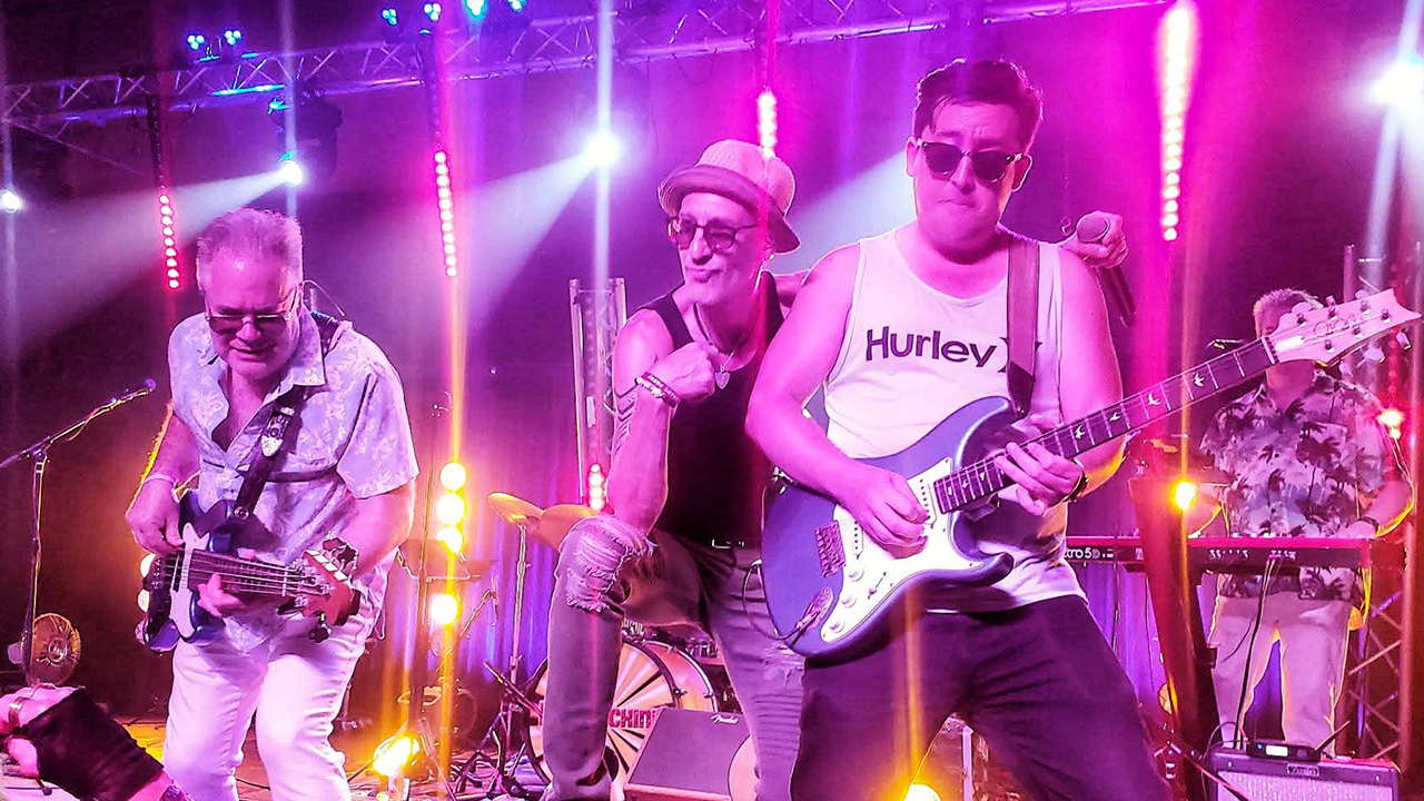 Three members of Hit Machine performing on a stage with bright lights.