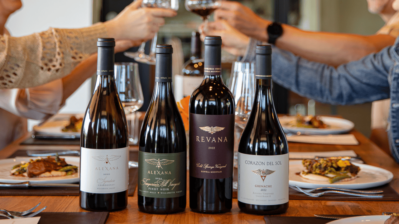 Four bottles of wine from Alexana Winery on a table with people in the background.