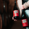 A woman holding two bottles of Lemelson Vineyard wine near wine barrels.