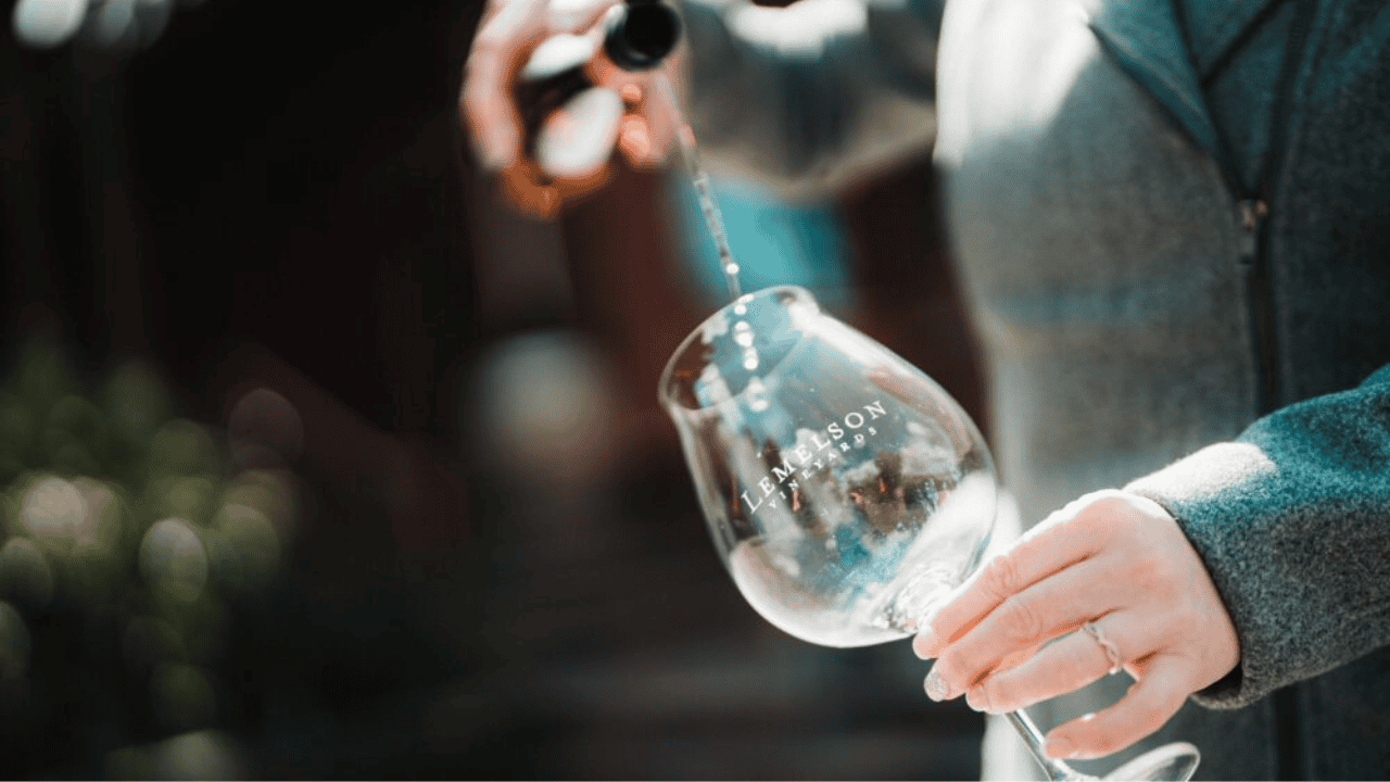 A bottle of wine poured into a glass with Lemelson Vineyard written on it.