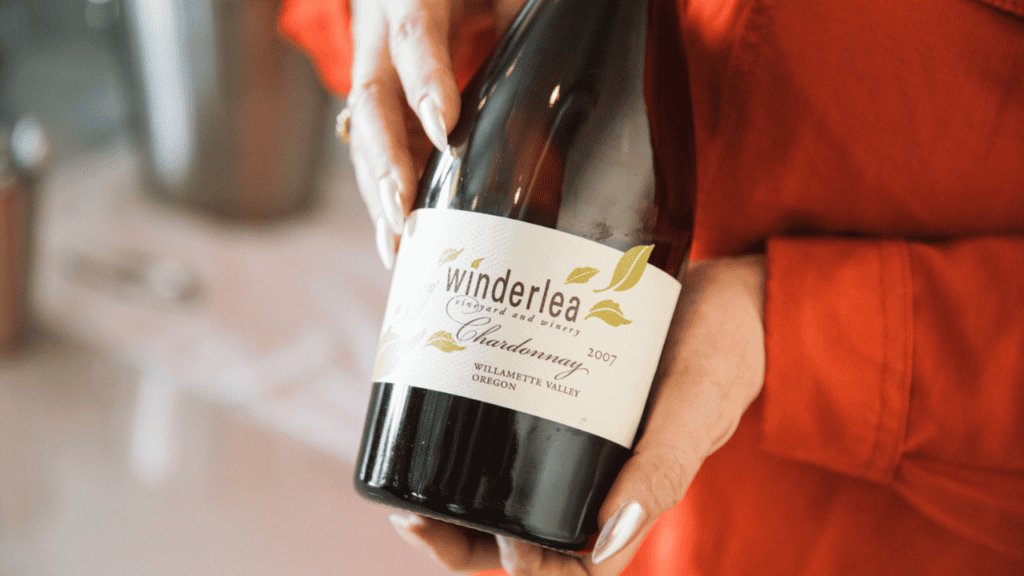 Two hands holding a bottle of Winderlea wine.