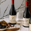 Four bottles of wine from Domaine Serene, with a wine glass and snacks.