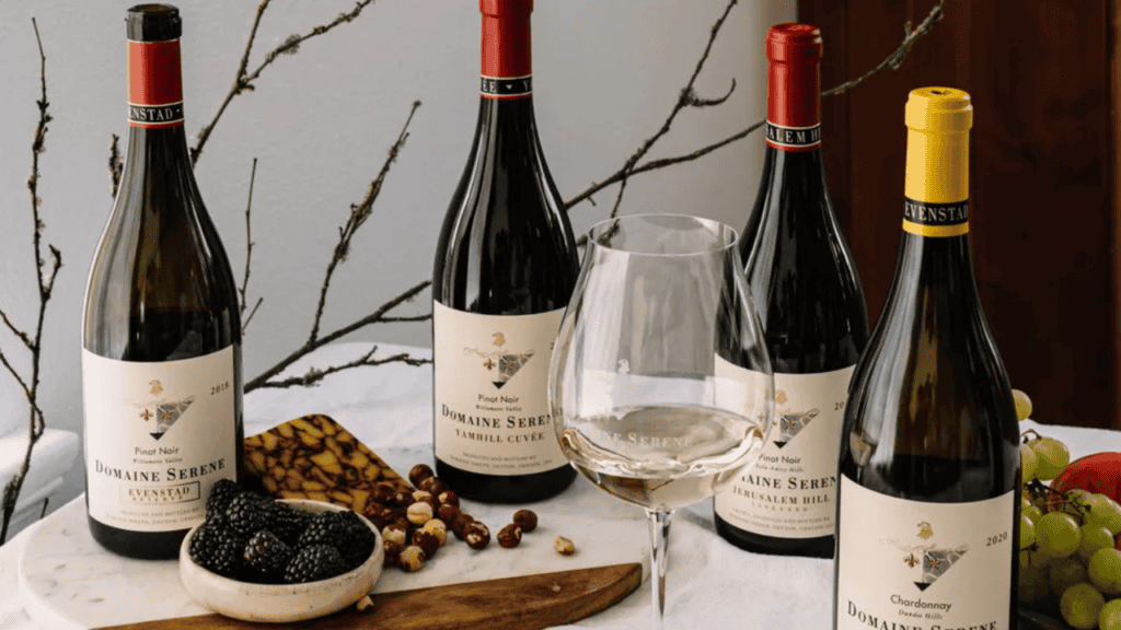 Four bottles of wine from Domaine Serene, with a wine glass and snacks.