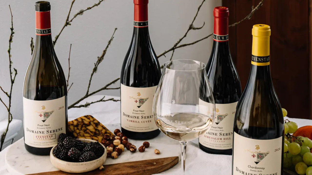 Four bottles of wine from Domaine Serene, with a wine glass and snacks.